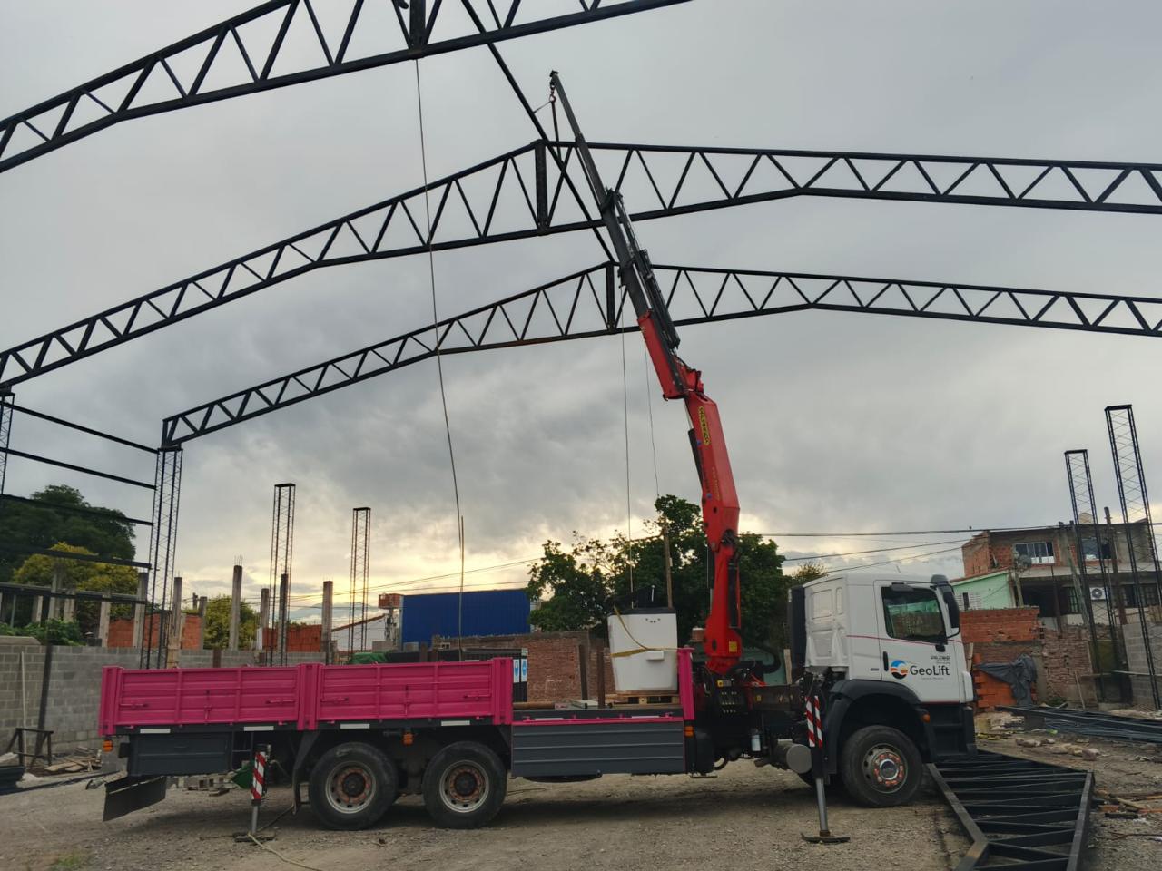 Hidrogrúa GeoLift con carrocería rosada izando carga en obra